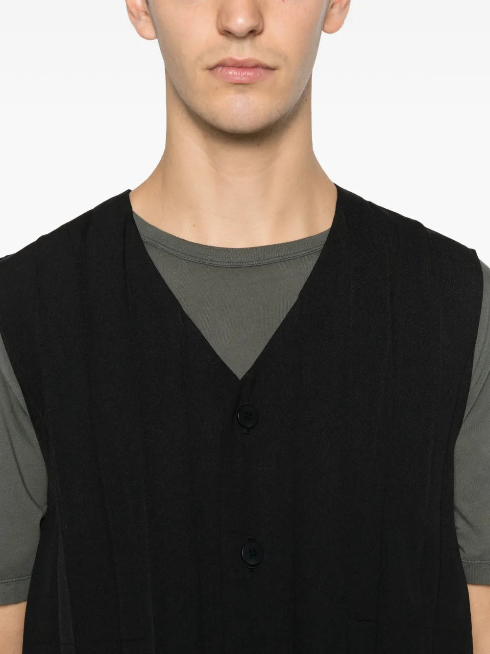 Close-up of the black plissé vest with front button closure from Homme Plissé Issey Miyake on a white background.