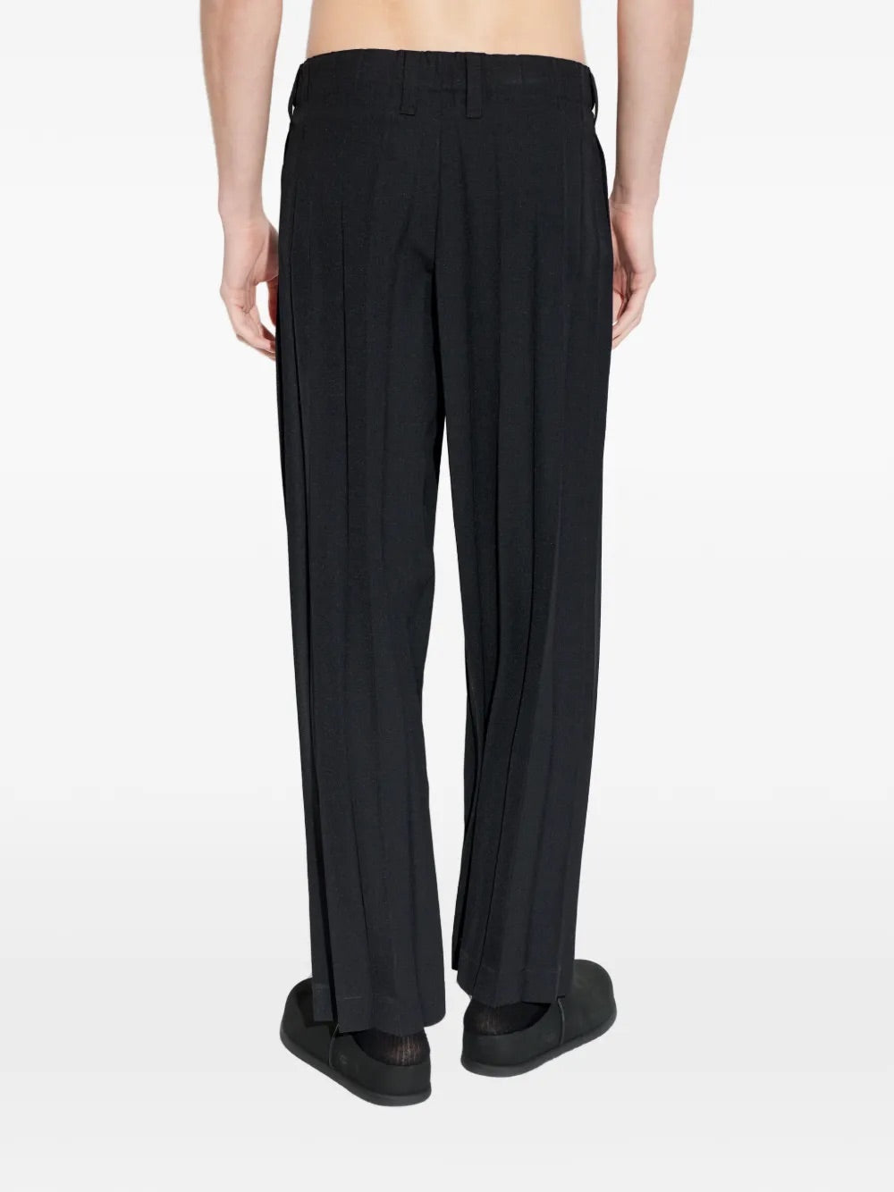 Model wearing Edge Ensemble Pants in Black by Homme Plissé Issey Miyake, full-length back view of slim-leg black plissé trousers