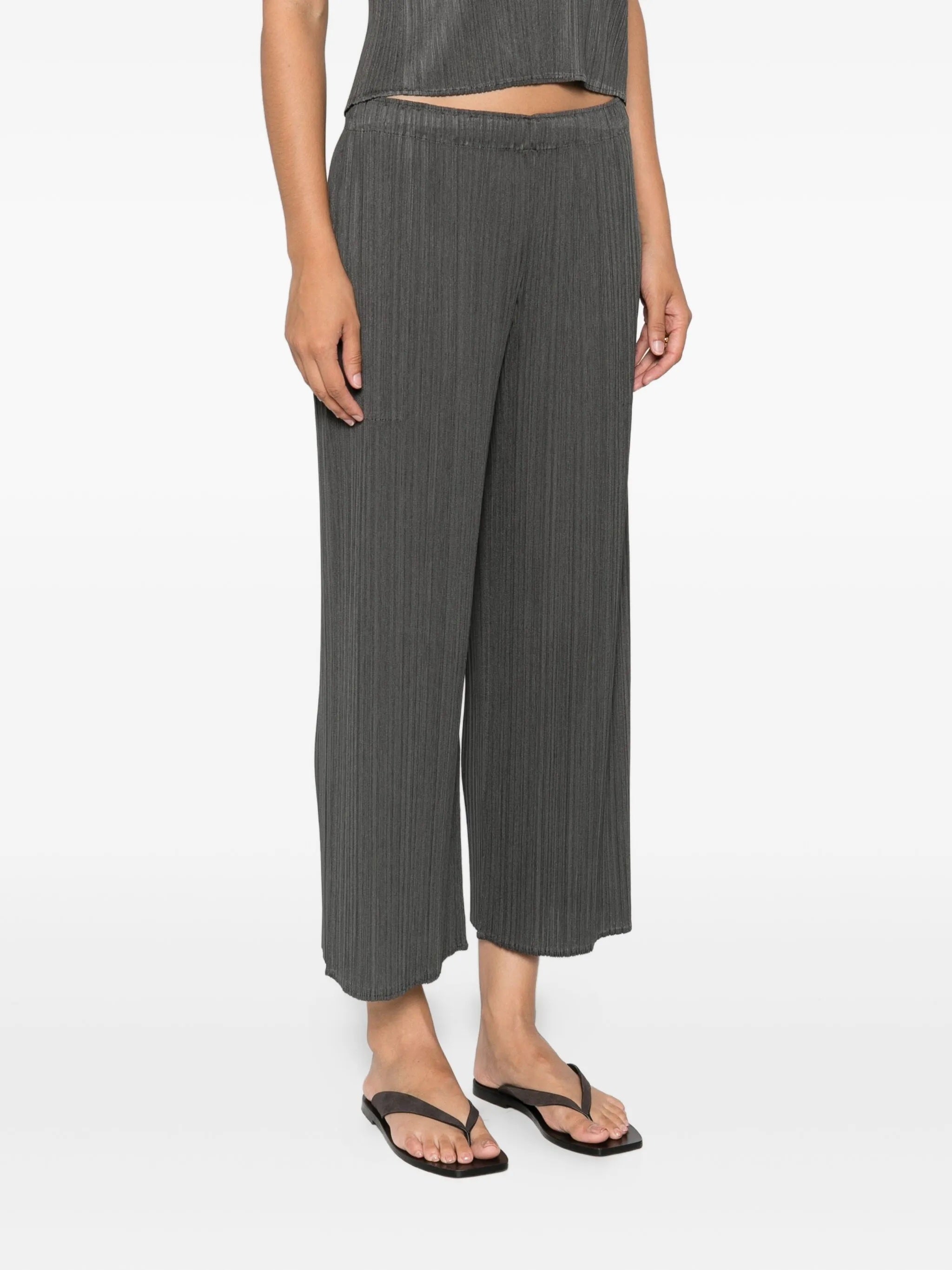 Woman wearing gray pleated pants from Pleats Please Issey Miyake on a white background