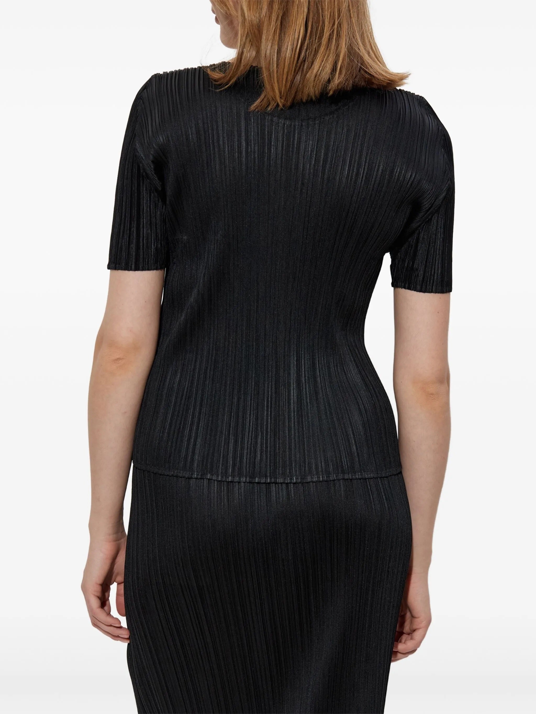 Black pleated top and skirt worn by a person on a white background