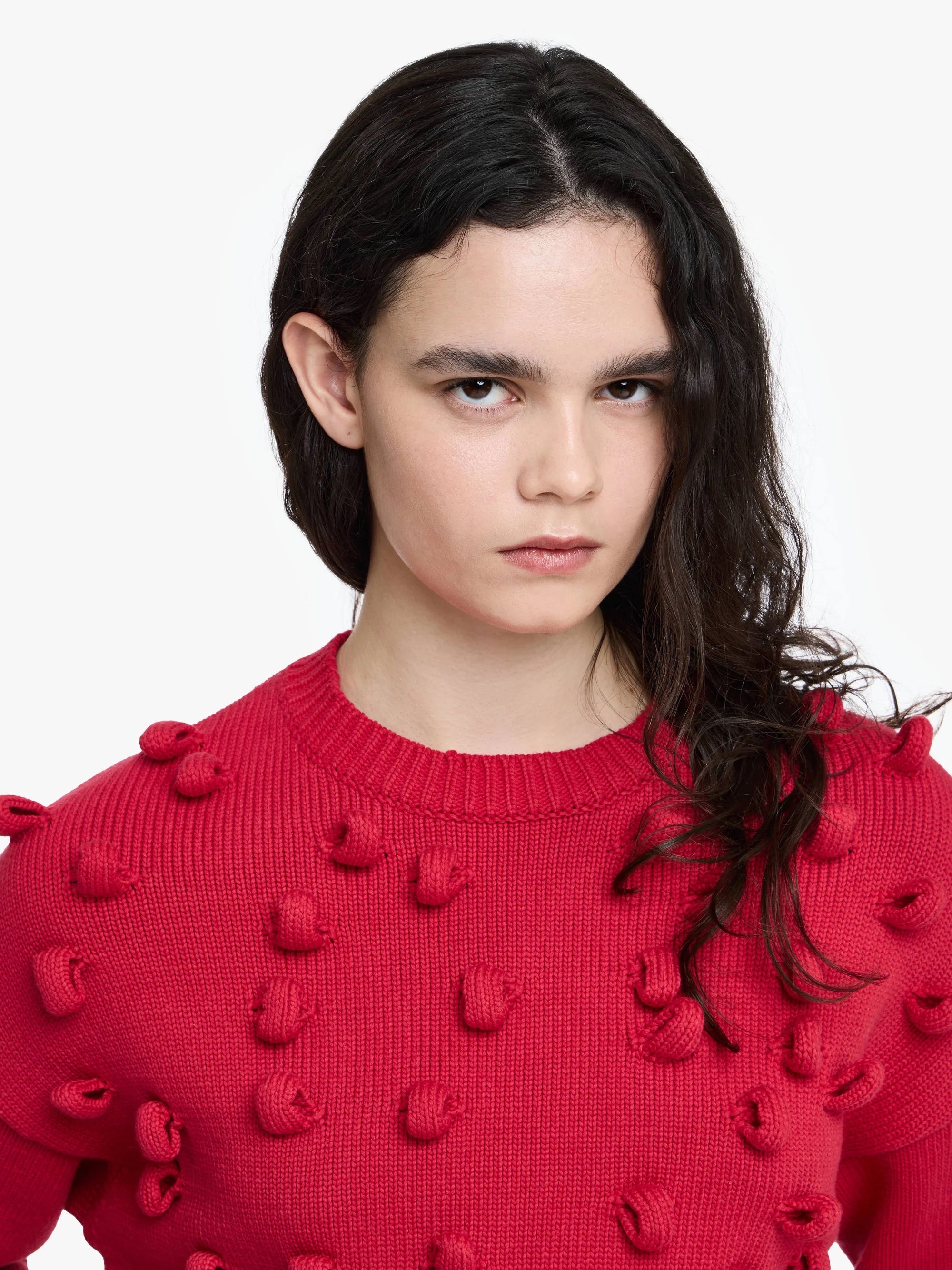 Person wearing a red sweater with pom-pom loops details on a white background