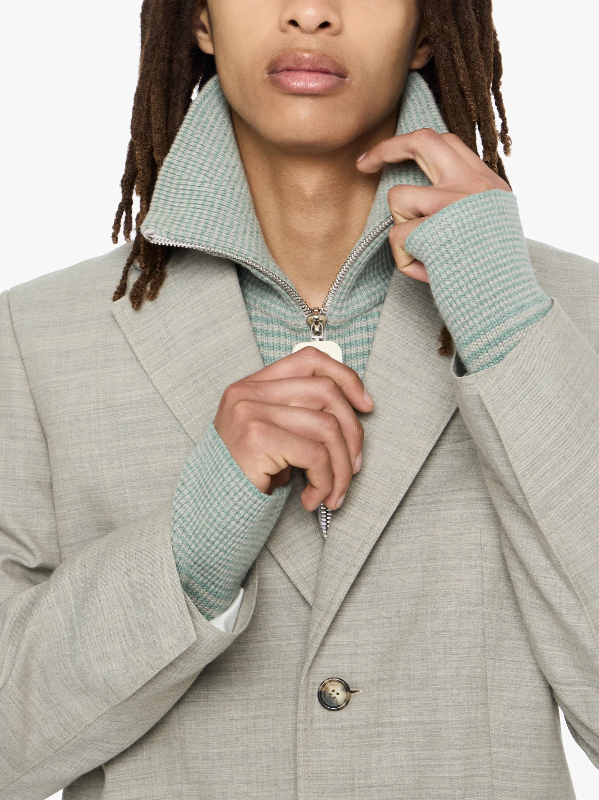Person wearing a light gray coat with a green sweater underneath, on a white background