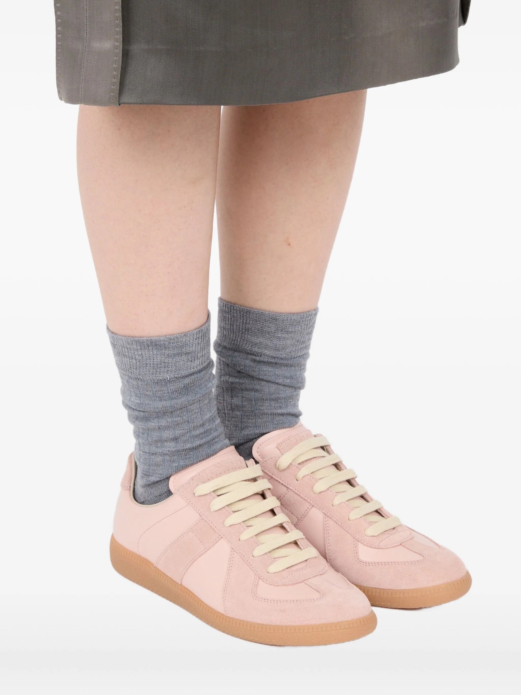 Someone wearing the soft pink leather sneakers with panel design from Maison Margiela on a white background