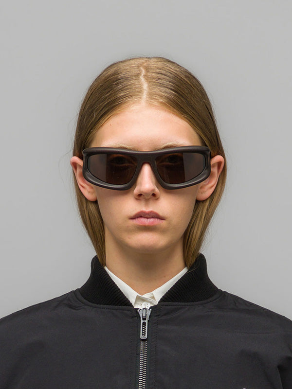 Mykita x 032c MARFA Sunglasses worn on model, front-facing model shot showing the bold ebony wraparound frame against the face, styled with a black bomber jacket and white shirt