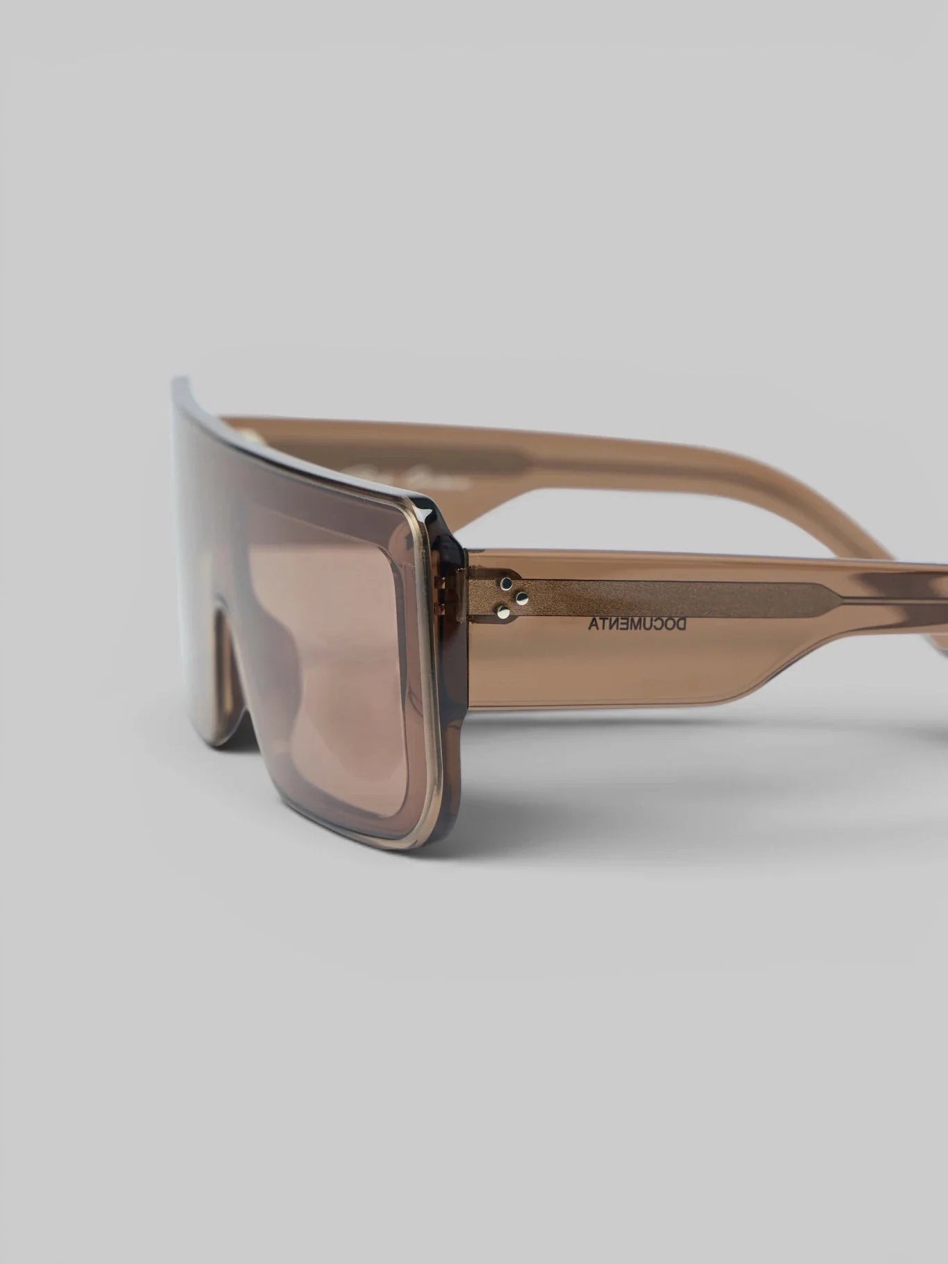 Three-quarter view of Rick Owens DRKSHDW Documenta Sunglasses showing glossy tobacco frame, transparent temples and wide brown-tinted lenses