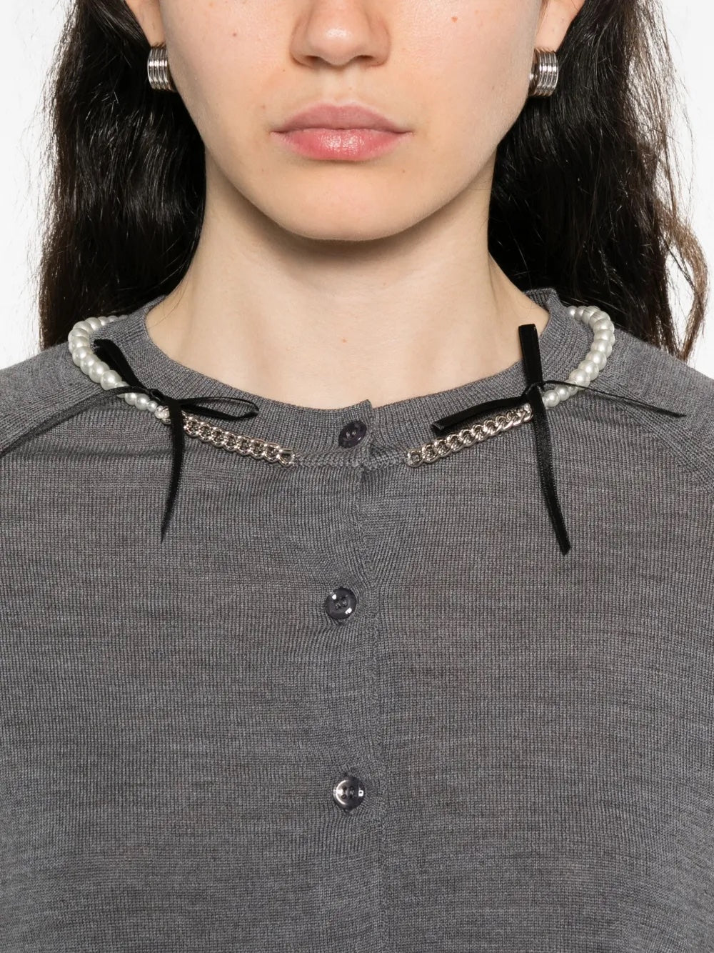 Close-up of a person wearing a gray cardigan with decorative black ribbons and pearl chain details.