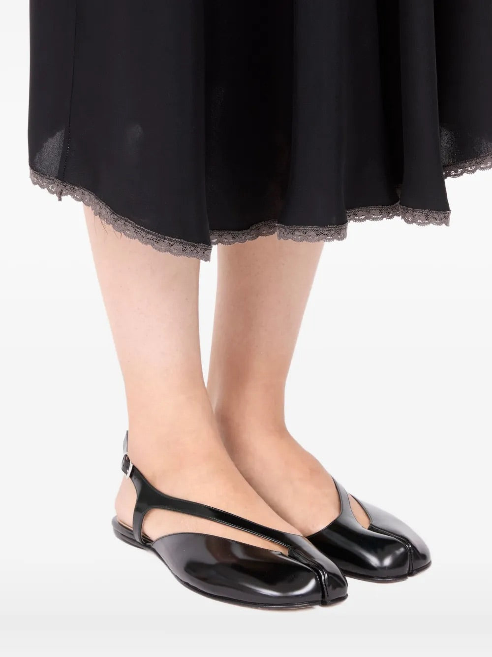 Diagonal front view of a model wearing the Maison Margiela Tabi Flat Slingback in black, emphasizing the signature split toe, flat sole, and modern slingback silhouette in a styled look.