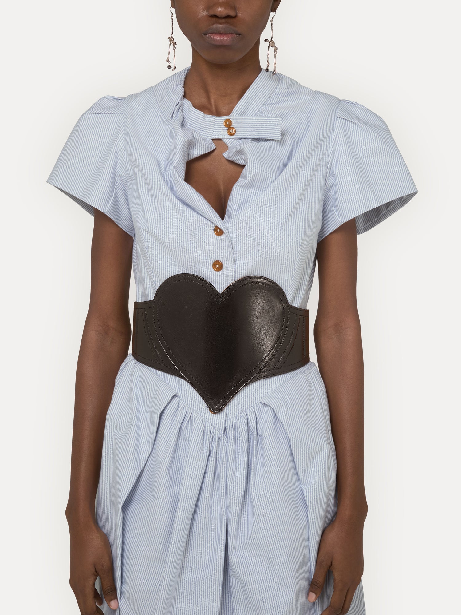 Model wearing Vivienne Westwood Heart Corset Belt in black over a light blue dress, showing waist-defining heart-shaped front