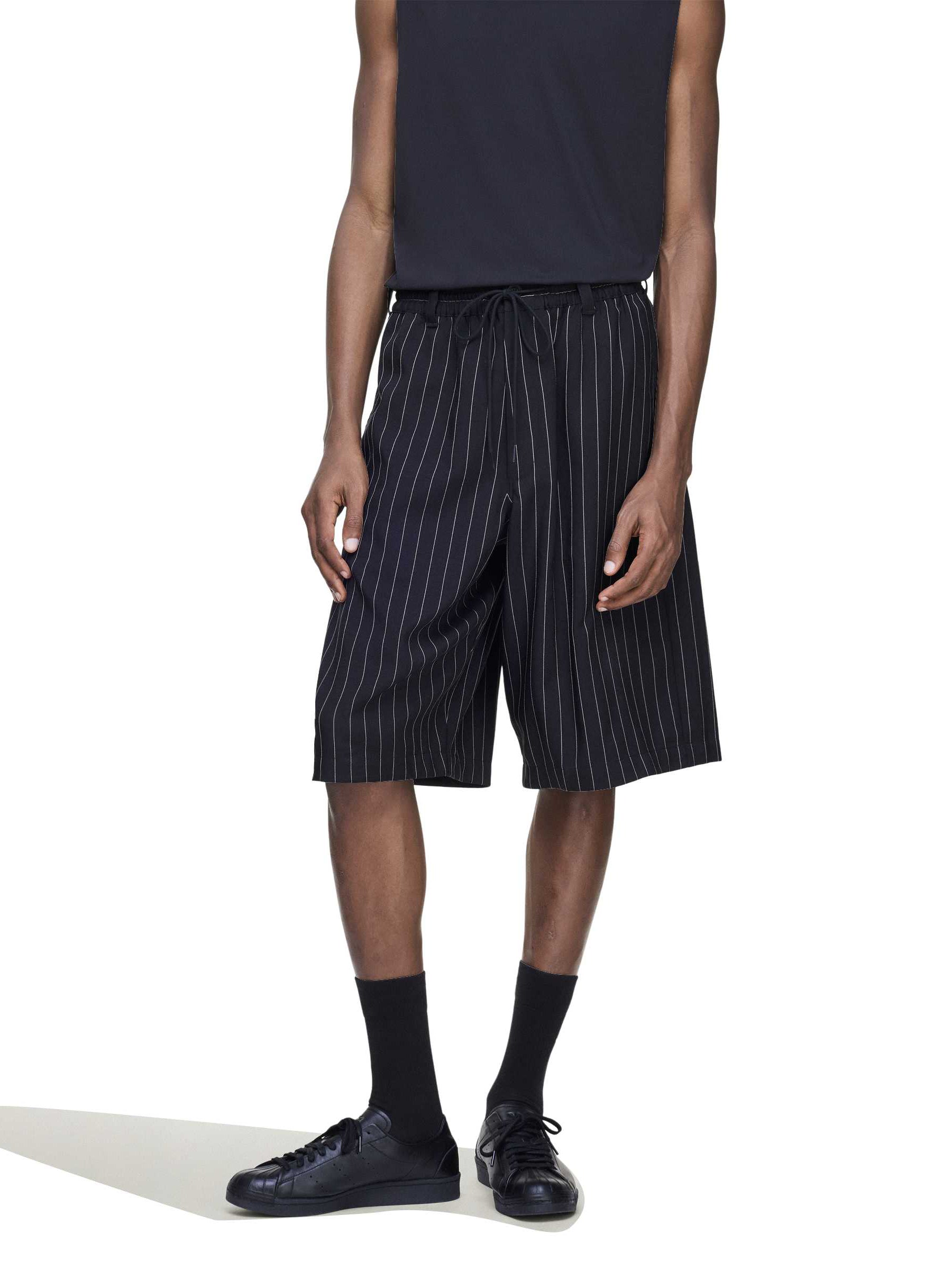 Close-up of a male model wearing the Y-3 Pinstripe Sport Uniform Shorts in Black, showing the pinstripe fabric and woven texture.