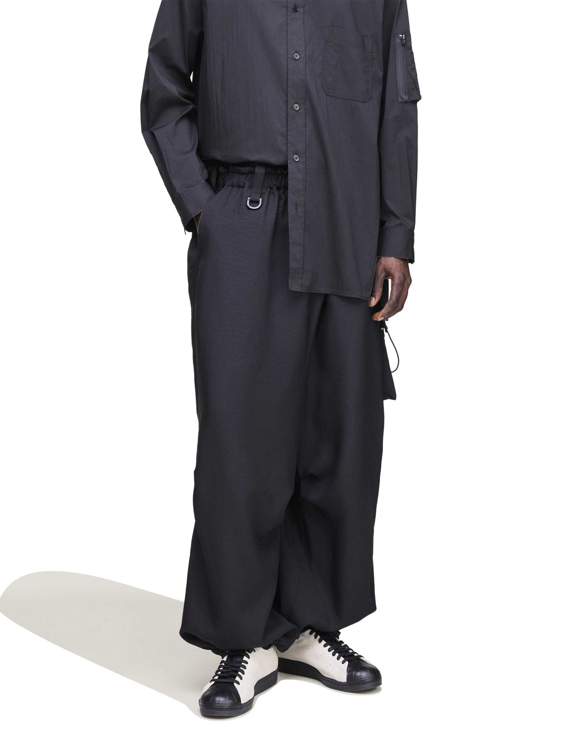 Close-up of the front of the Y-3 Sport Uniform Wide Cargo Trousers in Black on a female model, showing the integrated webbing belt with Fidlock® buckle and front fly.