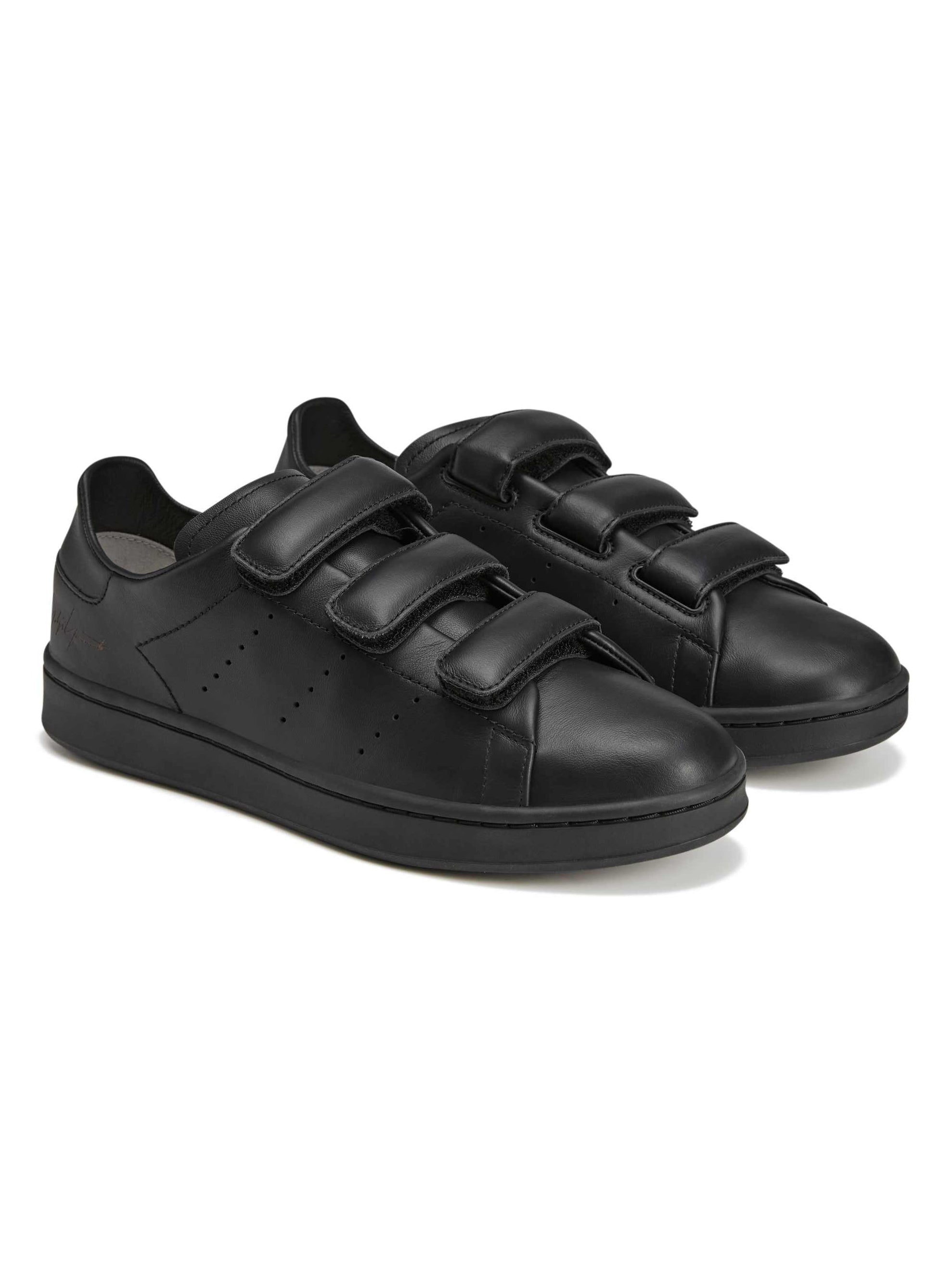 Diagonal packshot of the Y-3 Stan Smith Hook-and-Loop Shoes in Black, showing the leather upper, strap closure, and subtle Yohji Yamamoto signature near the heel.