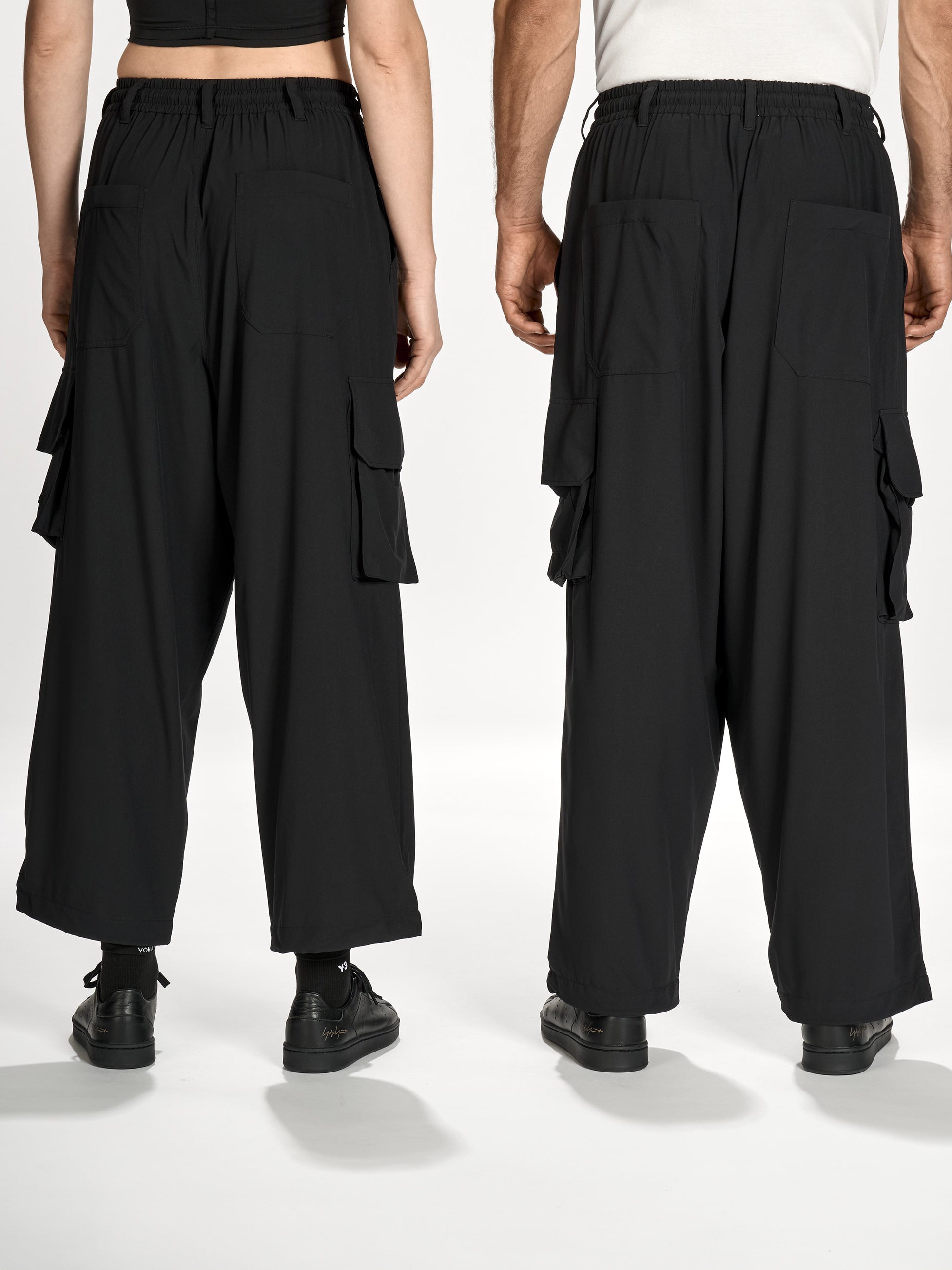 Back view of female and male models wearing Y-3 Utility Straight Tracksuit Pants in Black, showing the relaxed fit, straight-leg cut, and clean hem details.