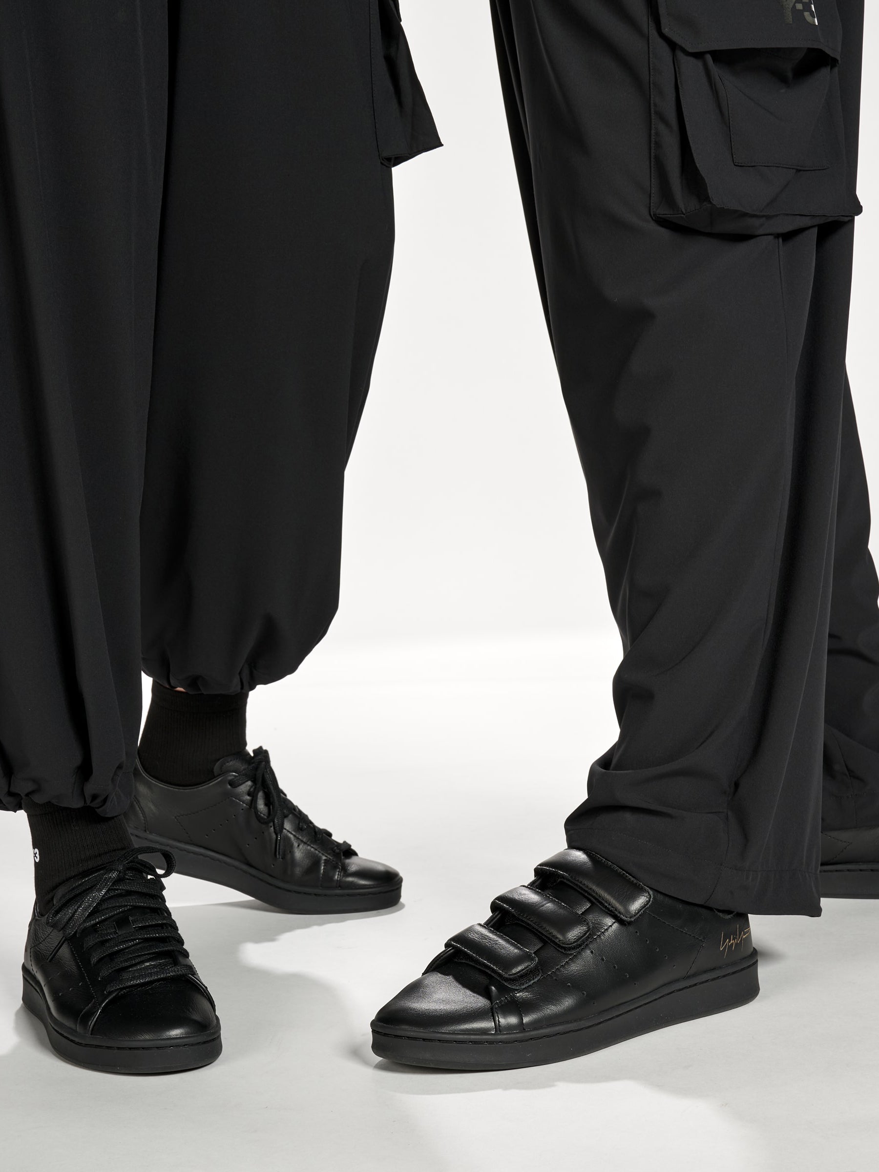 Close-up of female and male models wearing Y-3 Utility Straight Tracksuit Pants in Black, highlighting the fabric texture, straight-leg silhouette, and relaxed fit.
